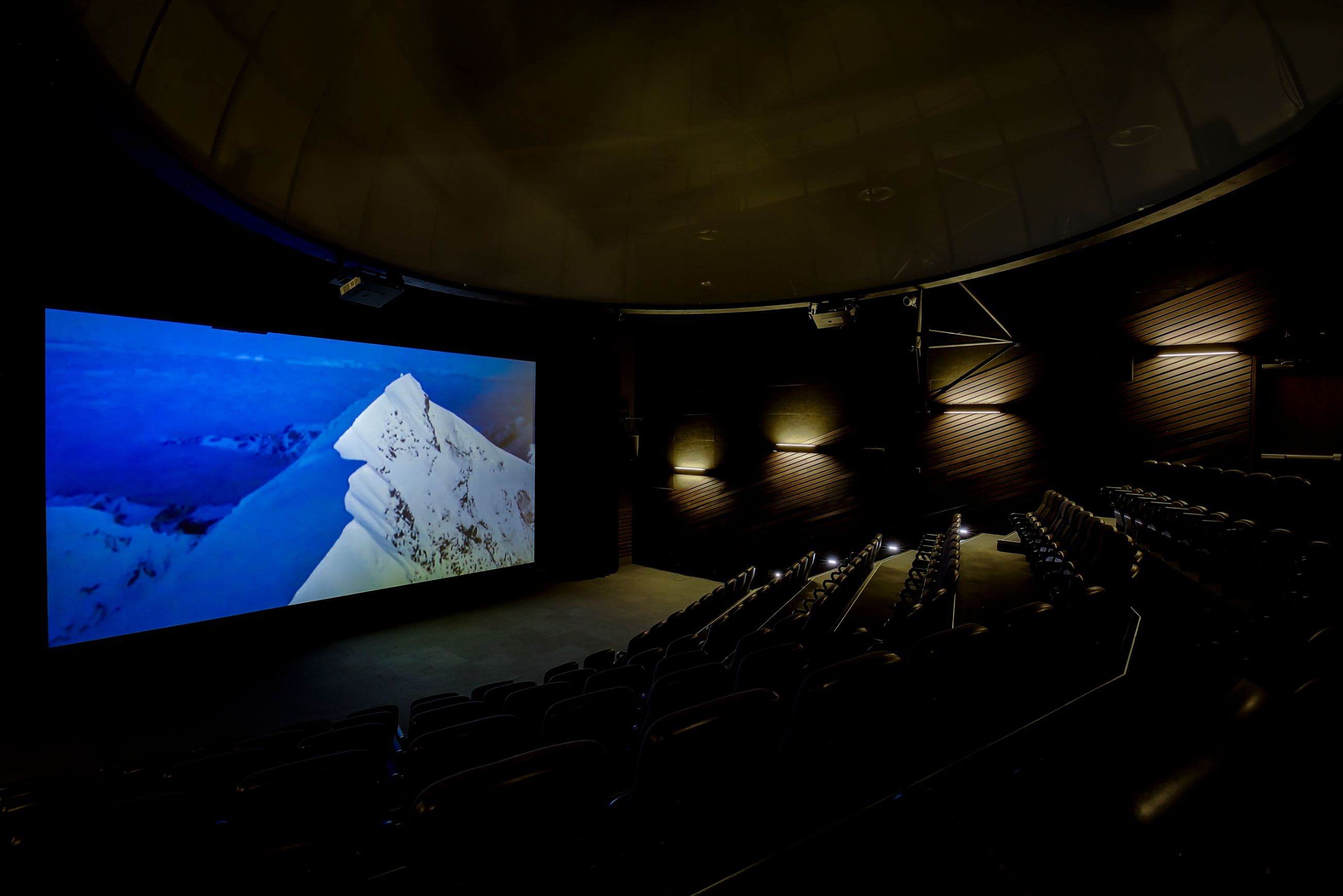 Empty dark movie theater showing a snowy mountain peak on a large screen.