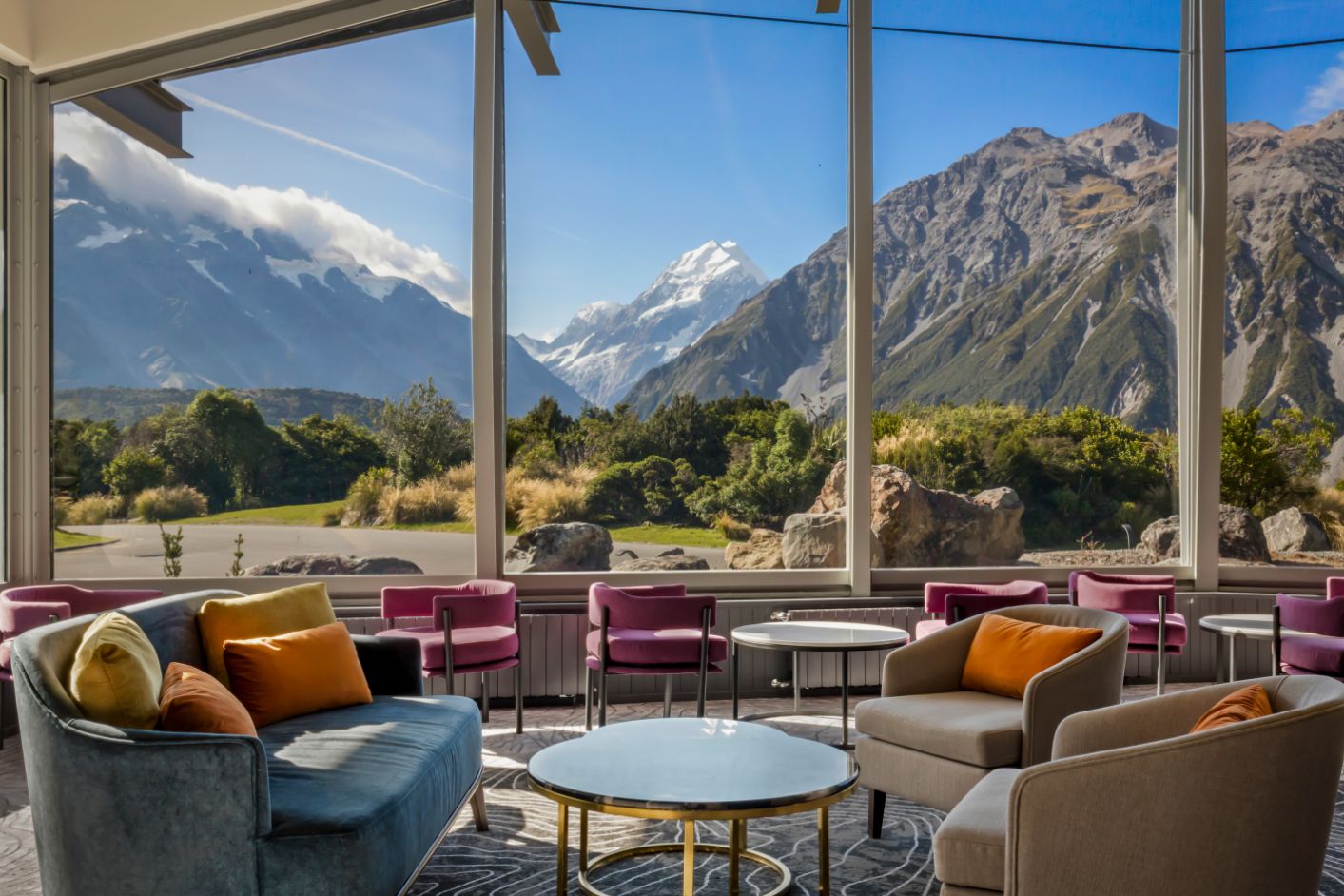 Lounge area with colorful chairs and sofa facing large windows showing a mountain landscape.